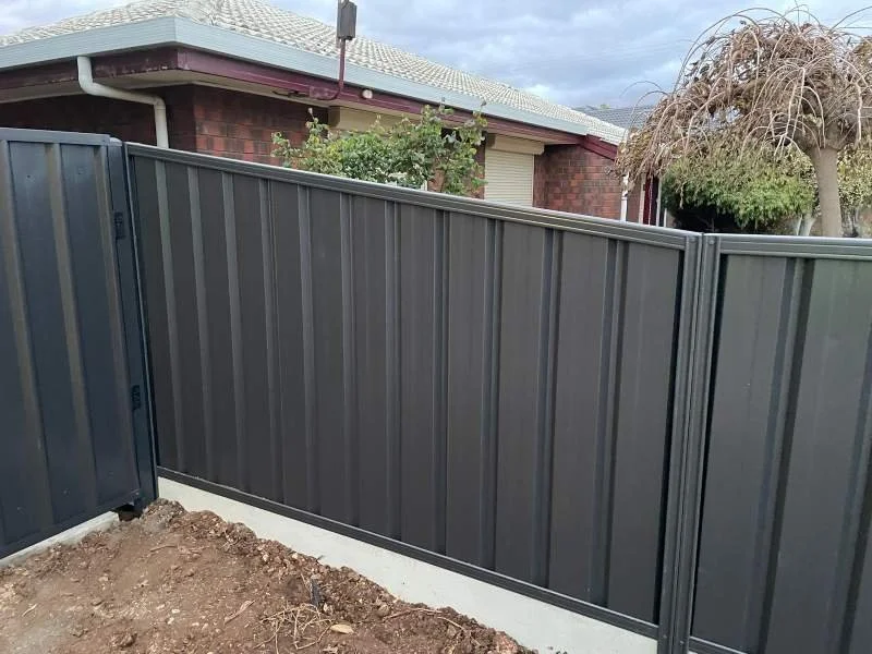 New gray metal fence installed in front of house with brick walls, bushes, and a tree.