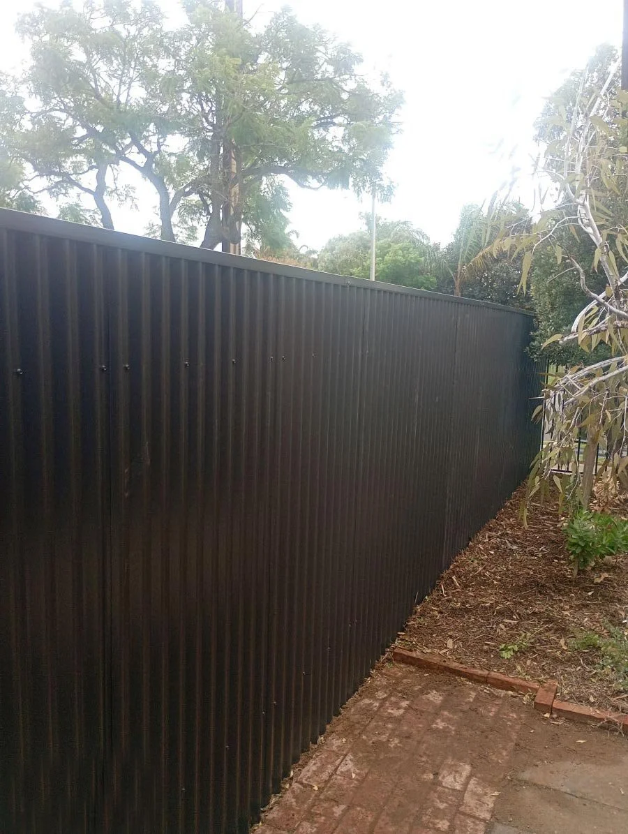 A black metal fence next to a brick pathway with trees and bushes in the background.