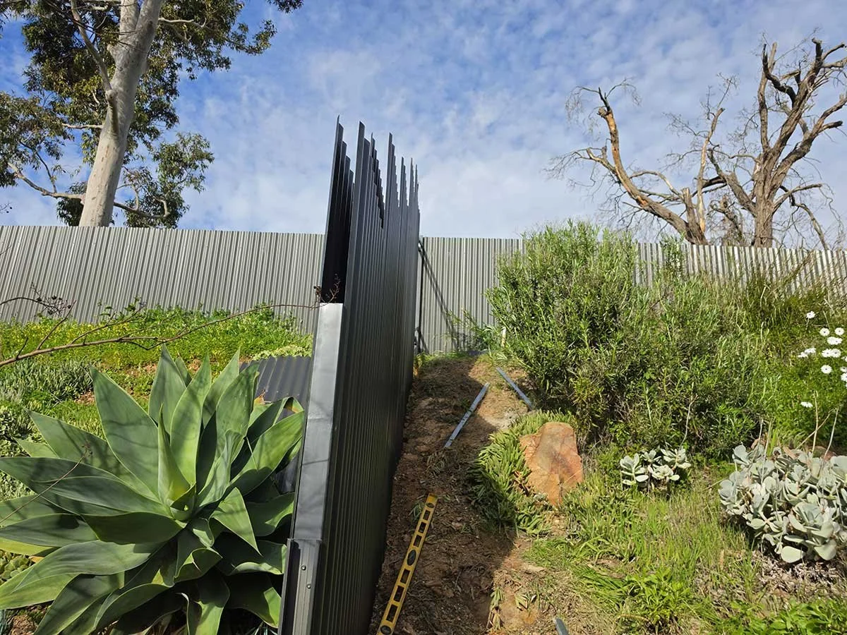 Post +rail twin fence in a very slope land grey color around bushes
