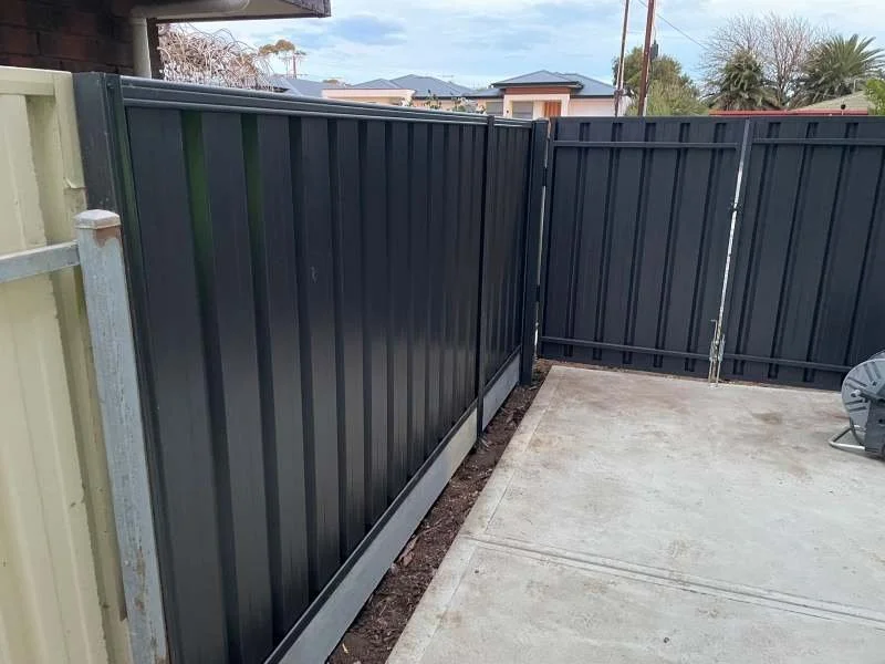 New black metal backyard fence installed next to concrete patio.