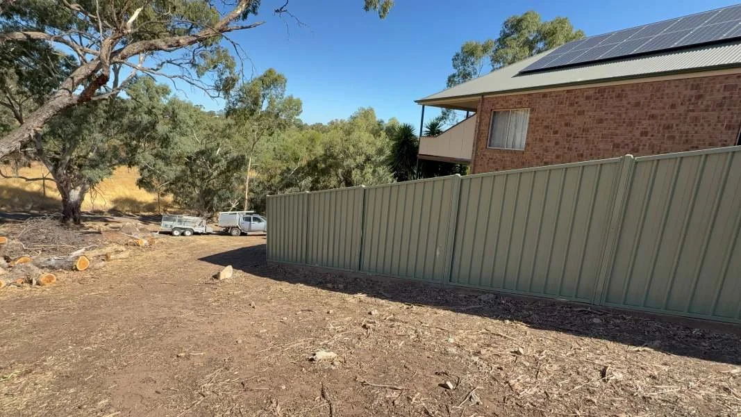 A backyard with a large metal fence, a two-story brick house with solar panels, and trees with a clear blue sky.