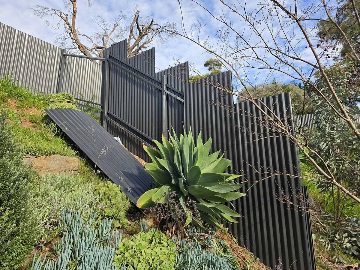 Post +rail twin fence in a very slope land grey color around bushes
