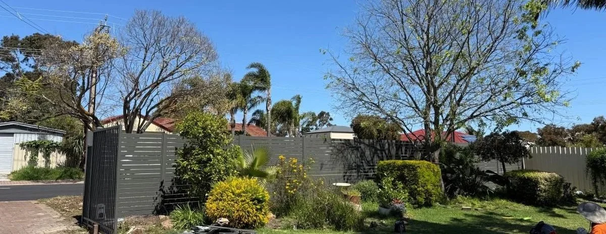 slat grey fence in garden with trees and  bushes