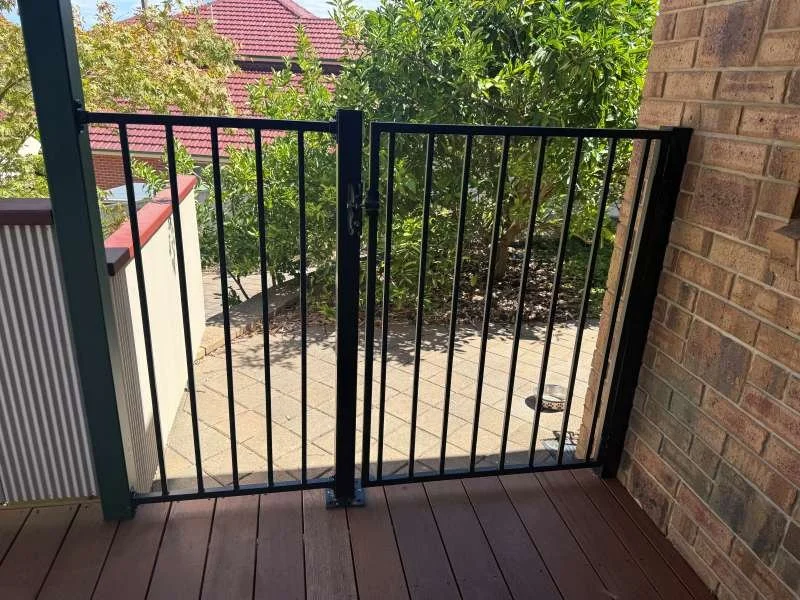 View from a balcony with black metal gate, greenery, paving stones, and part of a brick wall.