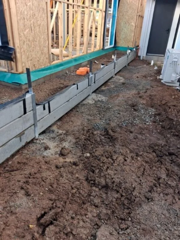 Construction site with concrete blocks and wooden framing for a building, with dirt ground in the foreground.
