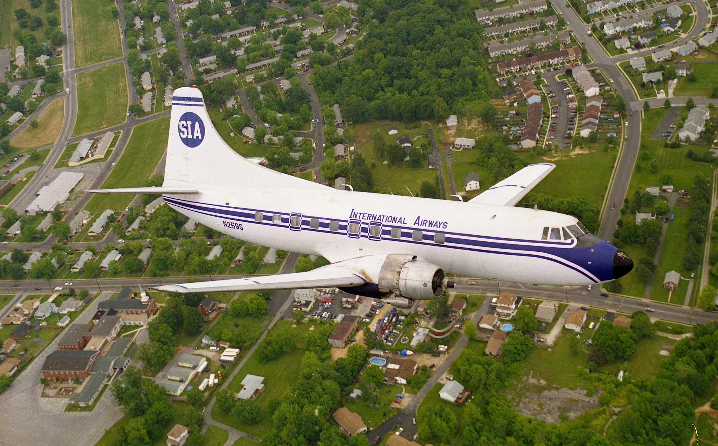 An airplane flying over a residential neighborhood with houses, trees, and streets.