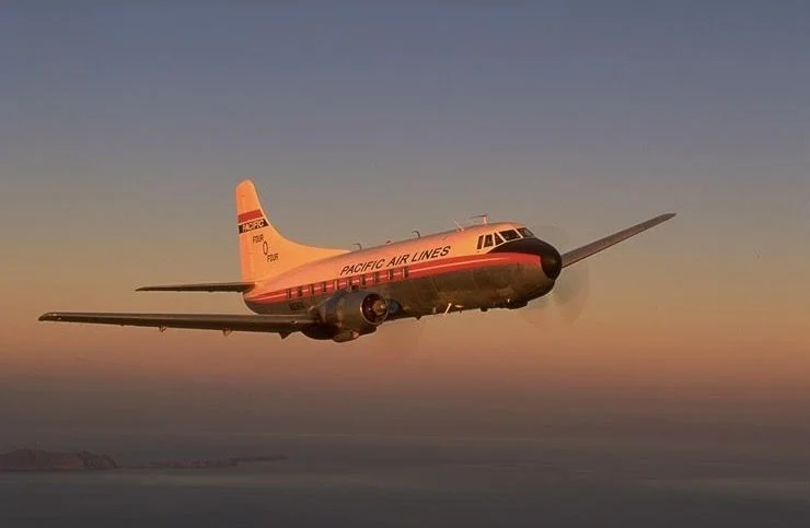 A vintage Pacific Air Lines airplane flying in a clear sky at sunset.