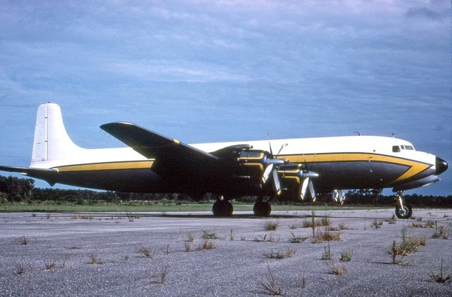A vintage propeller airplane on a runway under a partly cloudy sky.