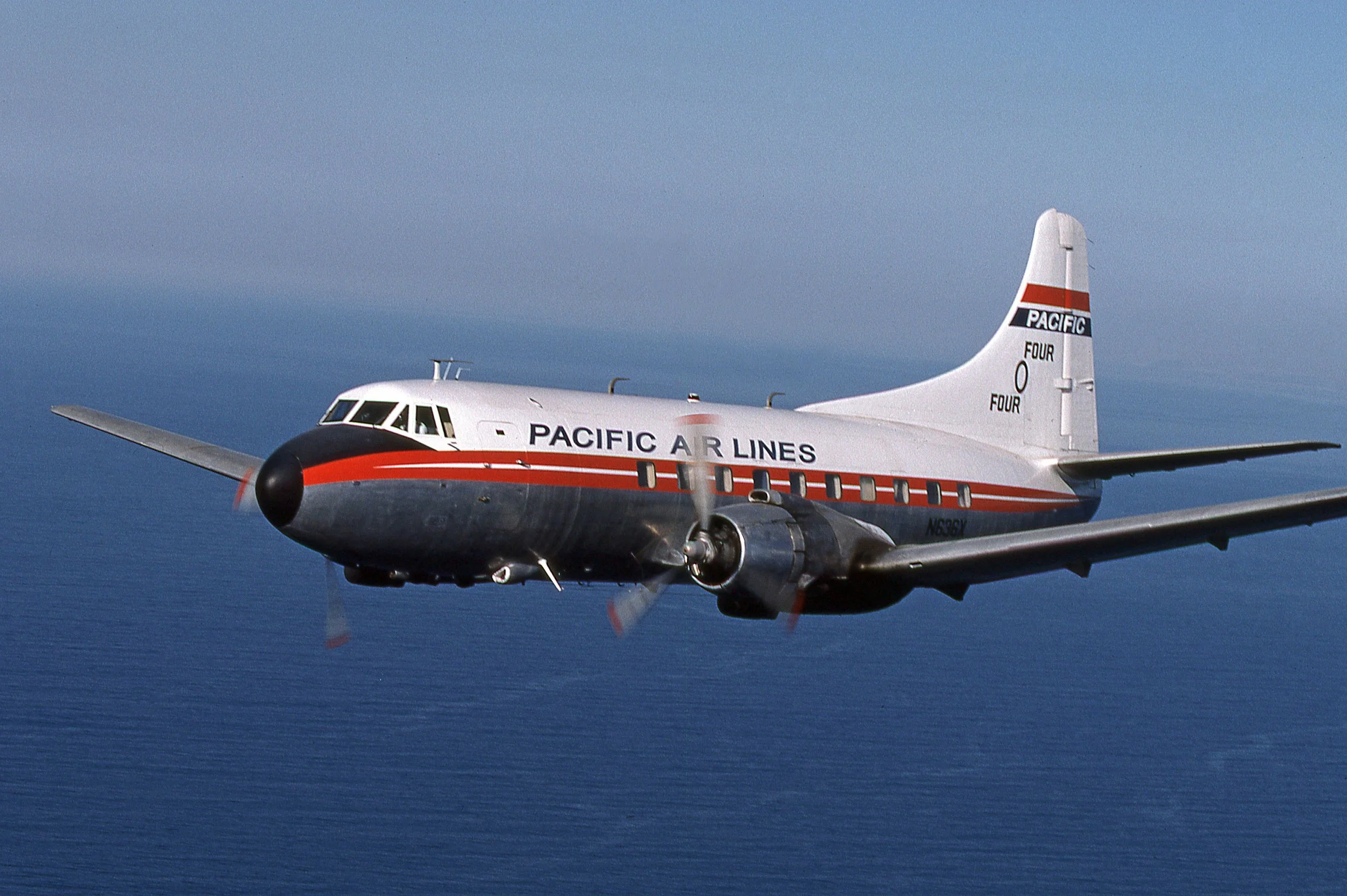 A vintage propeller airplane flying above the ocean with 'Pacific Air Lines' written on the side.