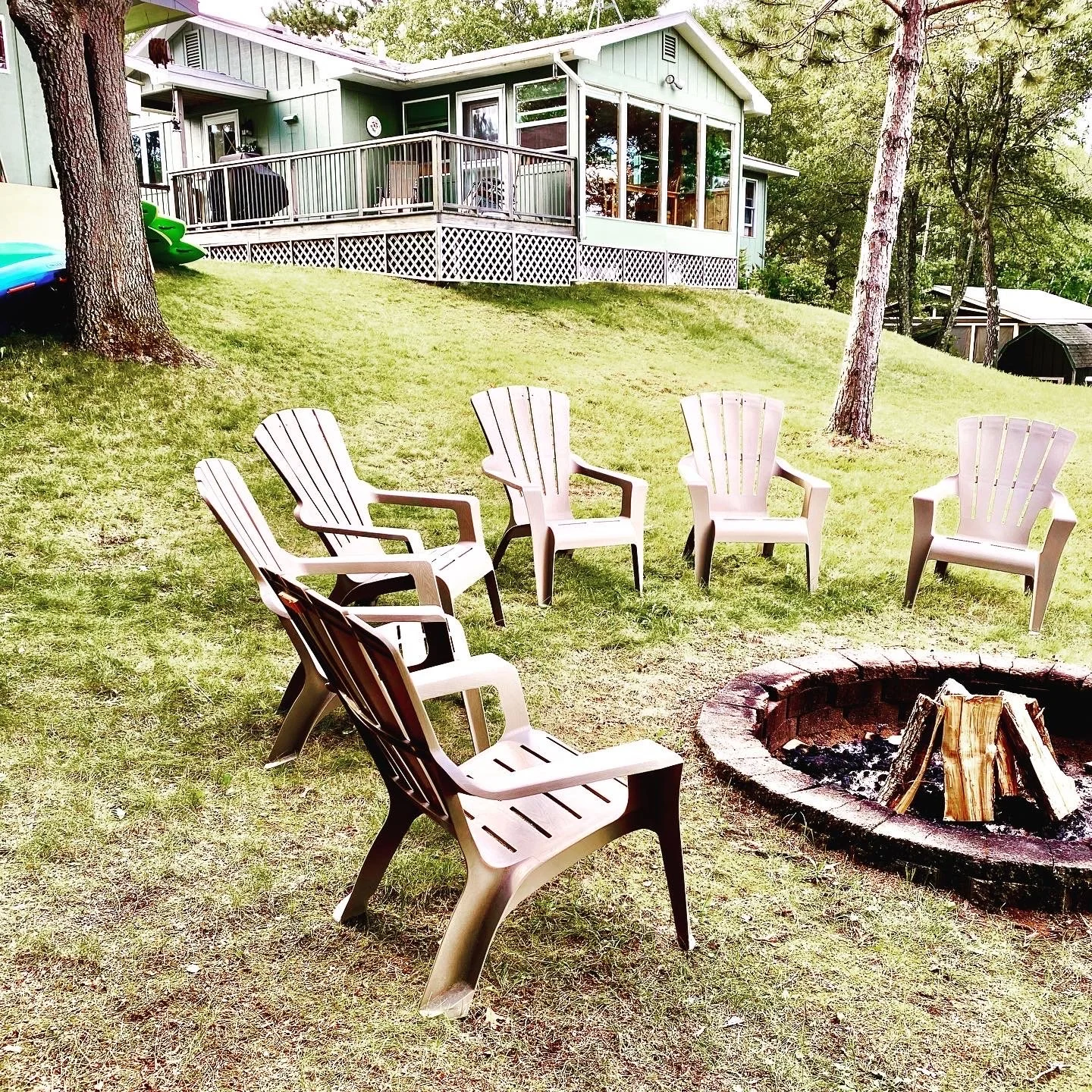 Adirondack chairs around stone fire pit on grassy lawn by Island Lake.