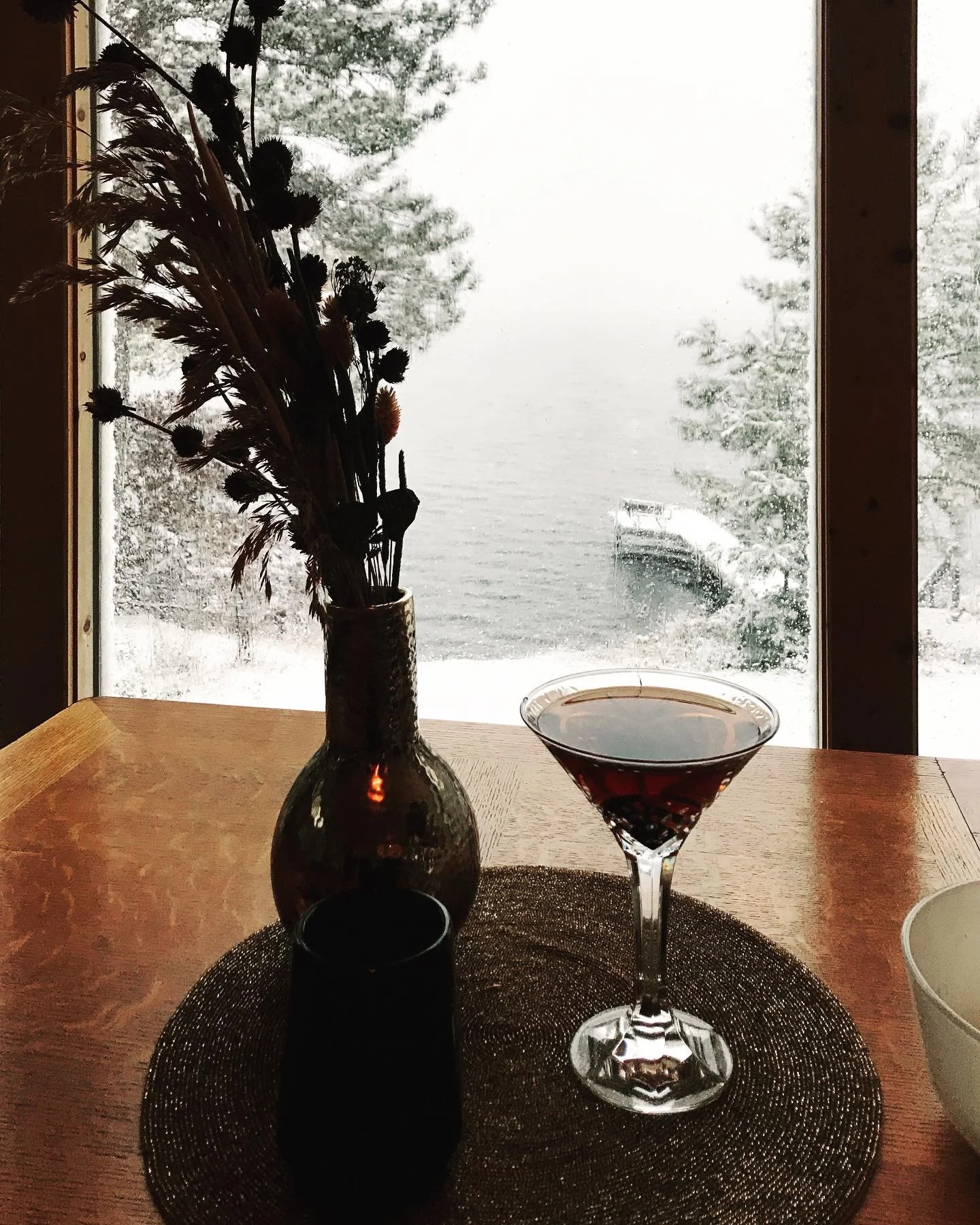 Two cocktails on table with snowy Island Lake view through window.