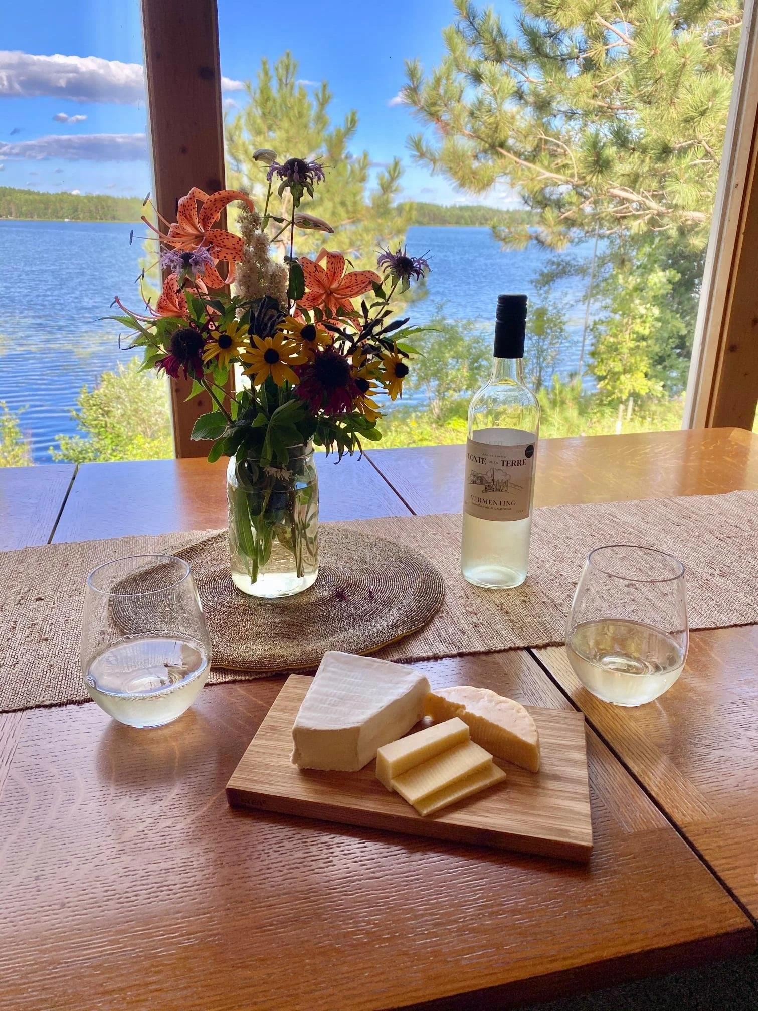 Wine and cheese setup on table with scenic Island Lake view in background.