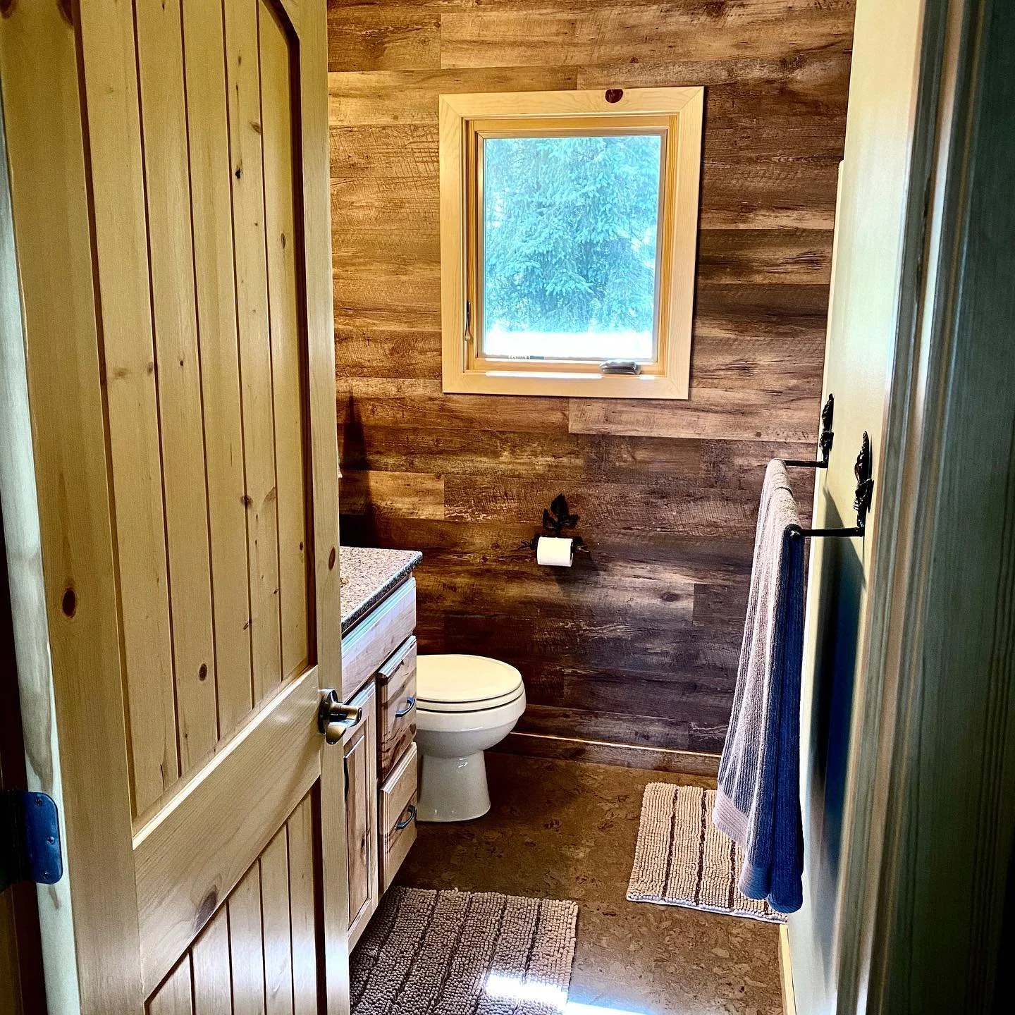 Cozy cabin bathroom with wooden door, vanity, and window view.