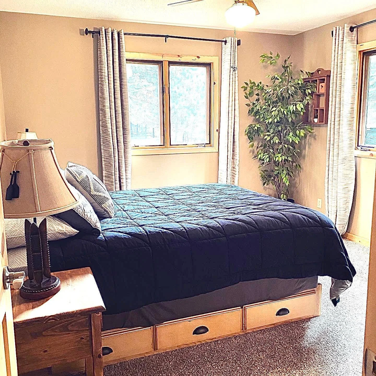 Cabin bedroom with dark comforter, wooden furniture, and window view.