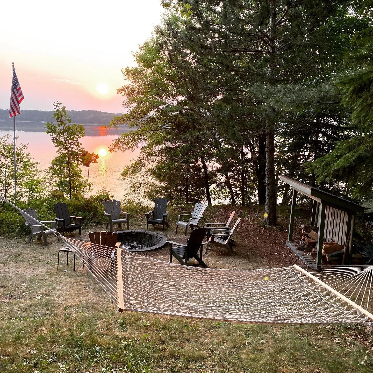 Lakeside fire pit area with Adirondack chairs and hammocks overlooking Island Lake.