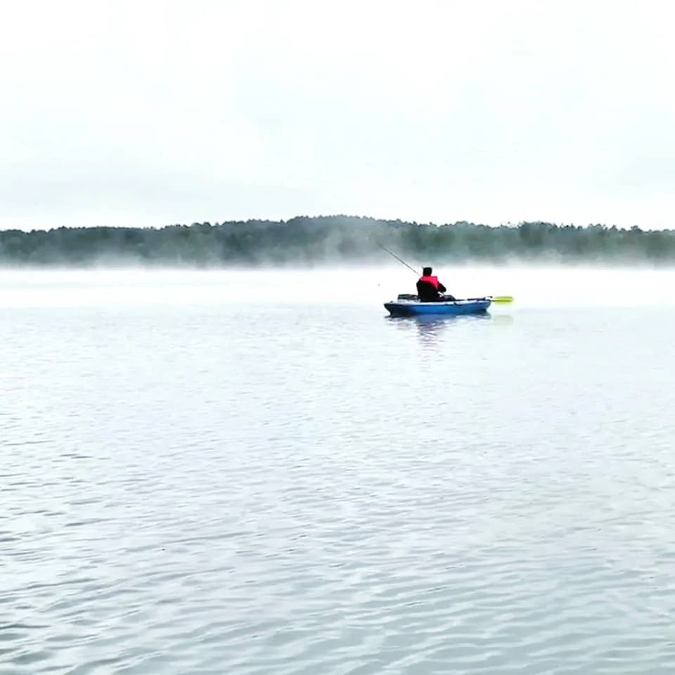Kayaker paddling on mist-covered Island Lake during early morning.