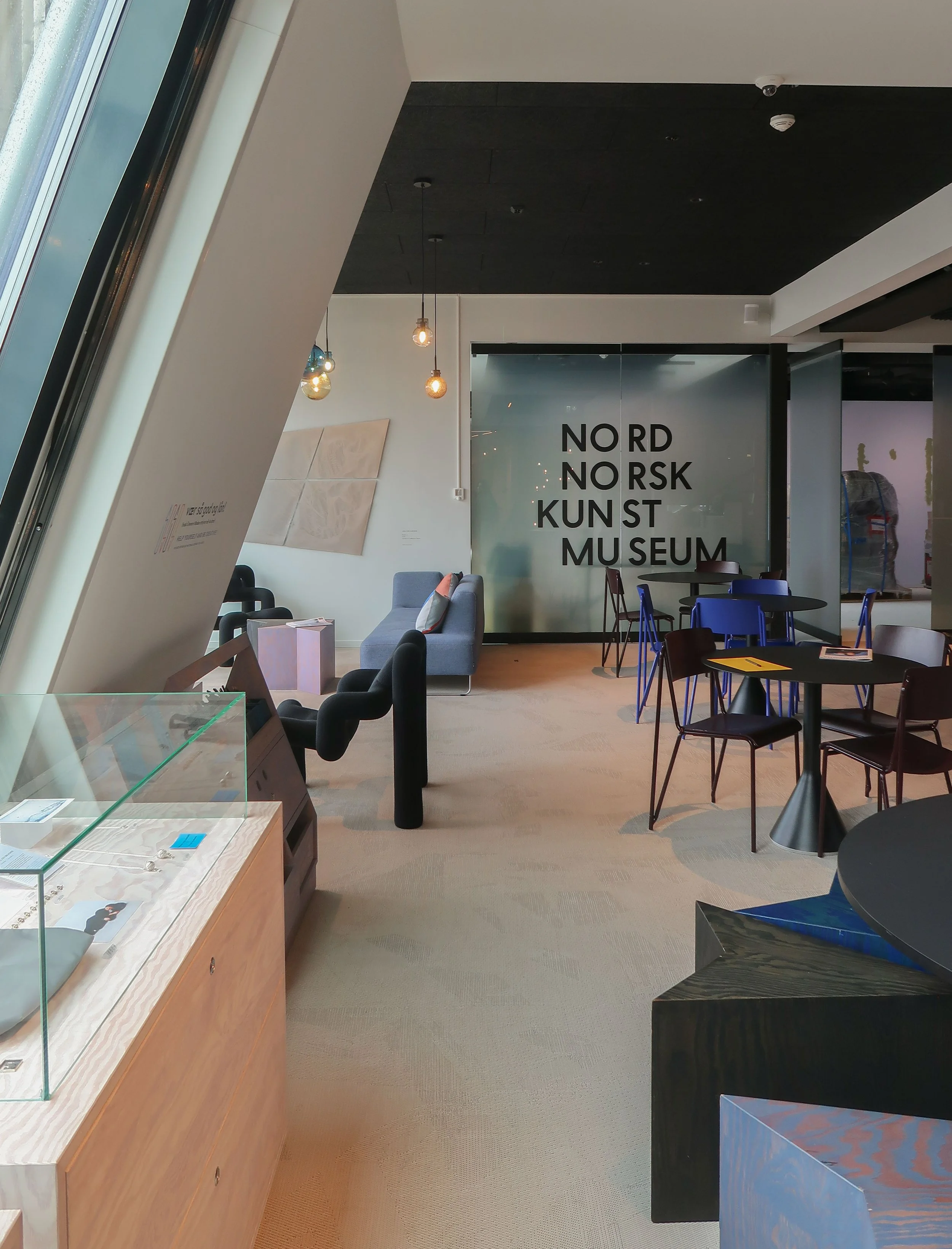 Interiør av Nord Norsk Kunstmuseum med lenestoler, bord og utstillingsgjenstander.