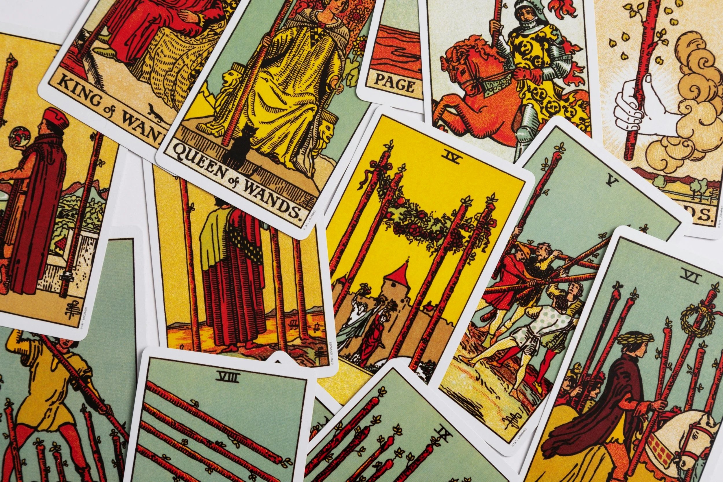 A scattered deck of Tarot cards, featuring the Tarot of Marseilles style, with various cards visible including the King of Wands, Queen of Wands, Eight of Wands, and the Page of Wands.