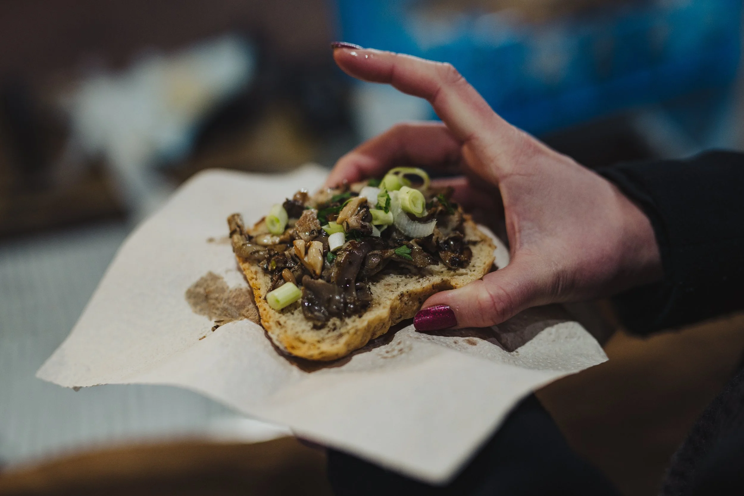 A person holding a slice of bread topped with cooked mushrooms and chopped green onions.