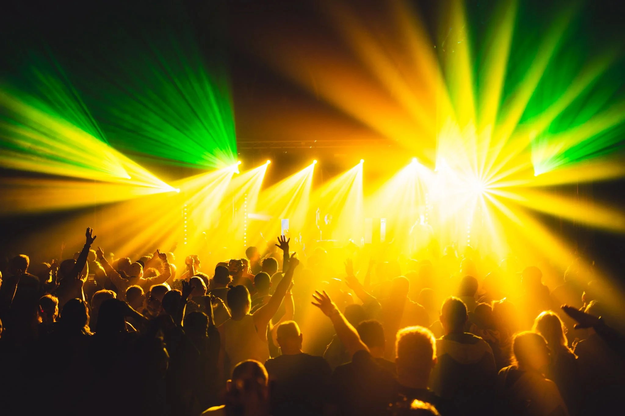 Crowd of people at a concert with bright yellow and green stage lights shining down.