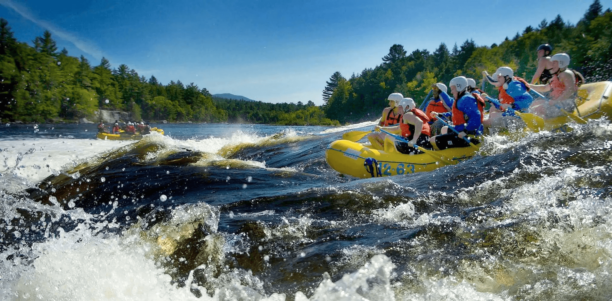 Group of rafters in helmets and life jackets navigating Class III whitewater rapids on the Kennebec River near The Forks, Maine