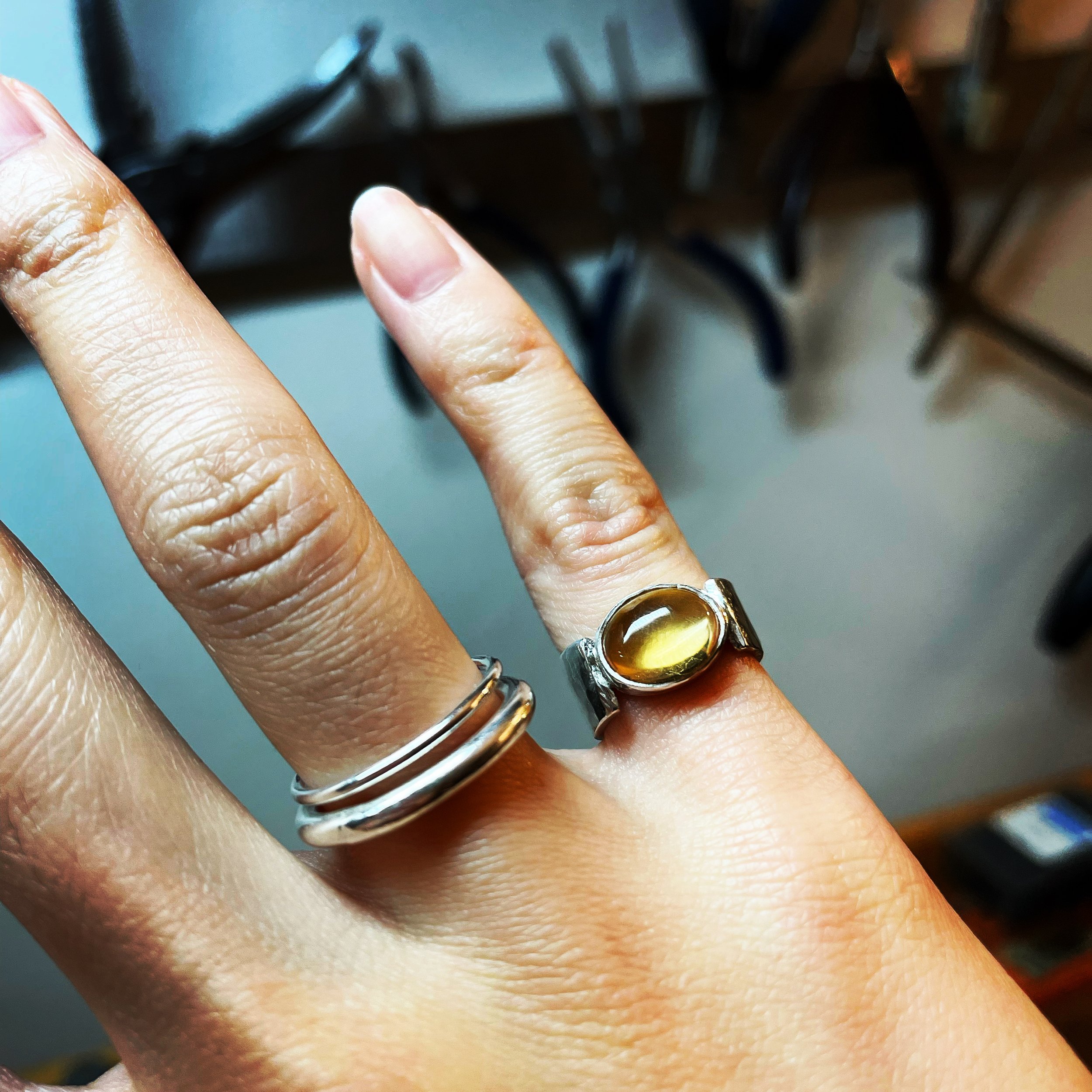 Hand wearing two rings, one with a yellow stone, against a background of tools.