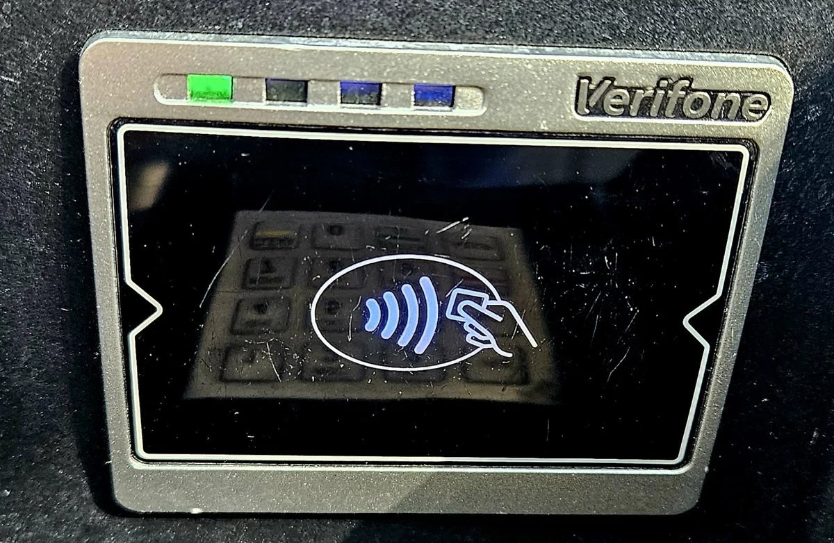 A contactless tap-to-pay reader with the wave and card symbol glowing on its screen