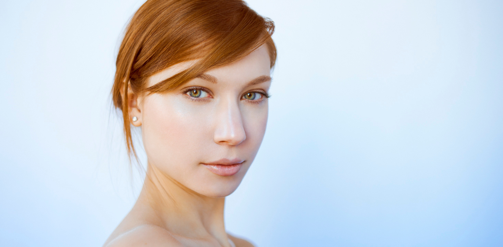 A redheaded woman with multicolored natural eyes stares directly into the camera against a popping blue background in this beauty shot by Nathanael Filbert. 