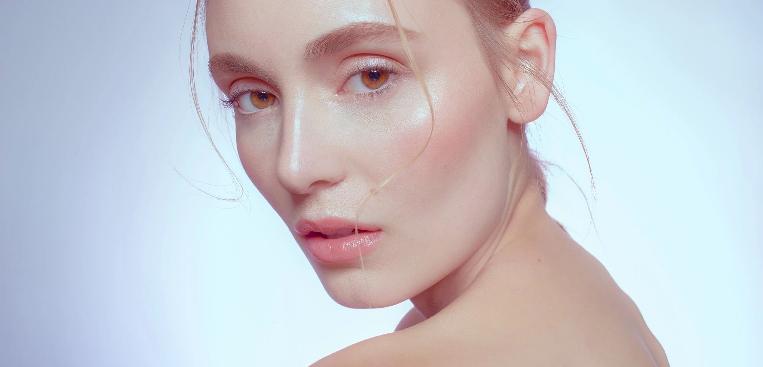 A model's cheekbone highlight and amber eyes people against a light blue backdrop in this beauty shot by commercial photographer Nathanael Filbert.