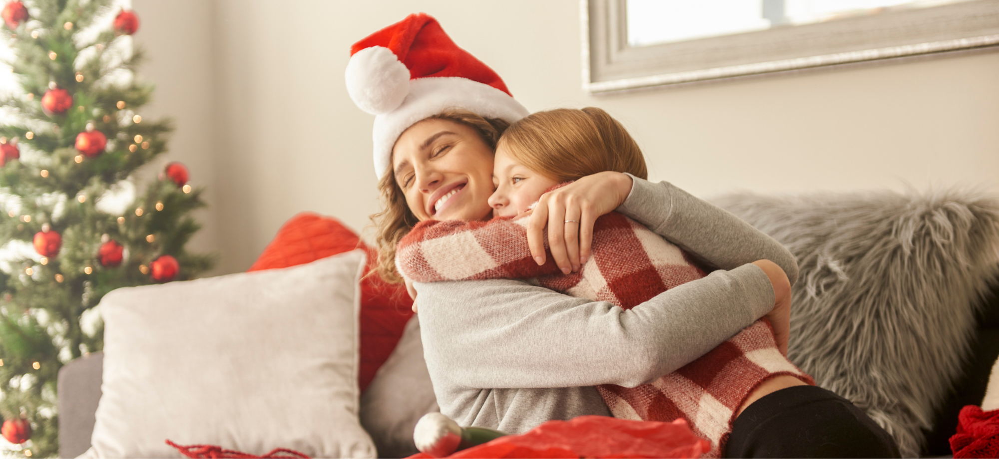 In a warm and bright living room a woman and young girl embrace after exchanging Christmas gifts. 