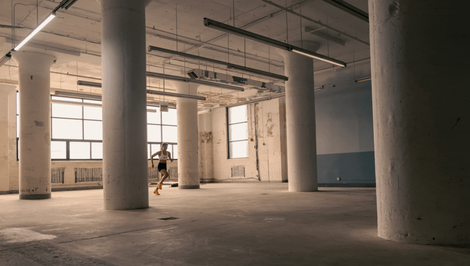 A GIF of a woman running through a wear house in a white sports bra, black shorts and neon orange shoes. 