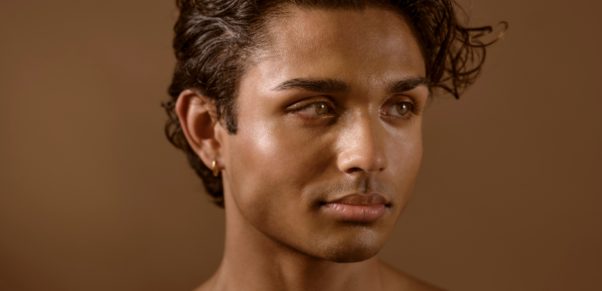 Man set against a backdrop that matches his skin tone. With dark hair and hazel eyes, he looks off camera. Photo by advertising photographer Nathanael Filbert.