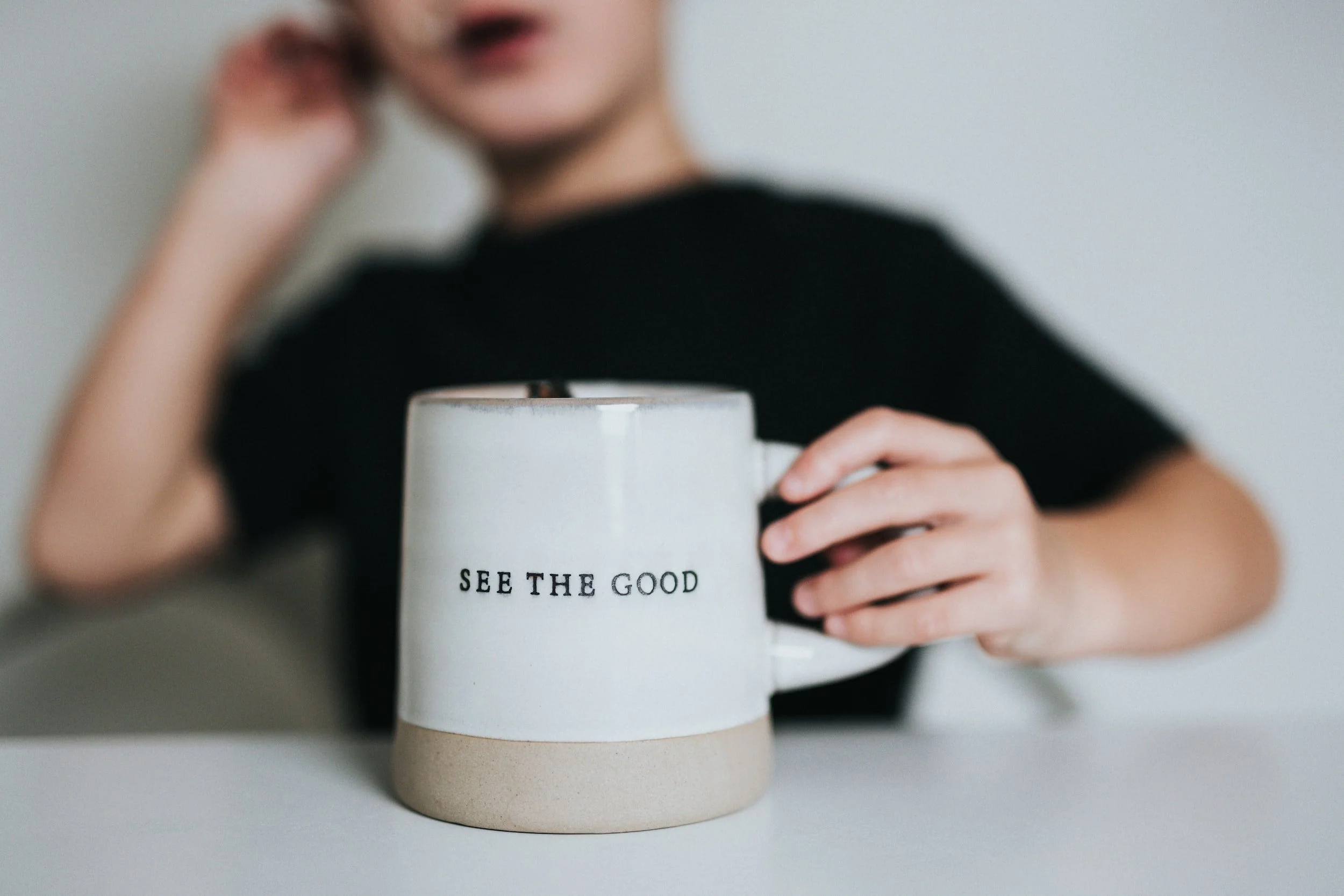 Child holding a mug with "See the Good" text.