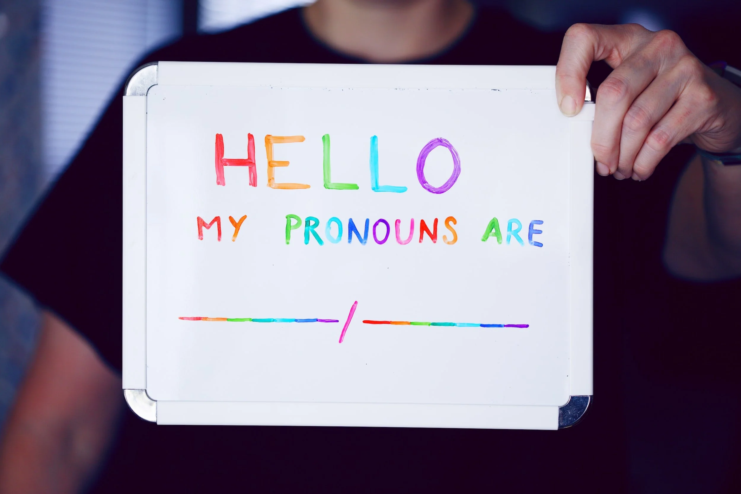 Whiteboard with text 'Hello, my pronouns are' in colorful letters and a blank line for input.