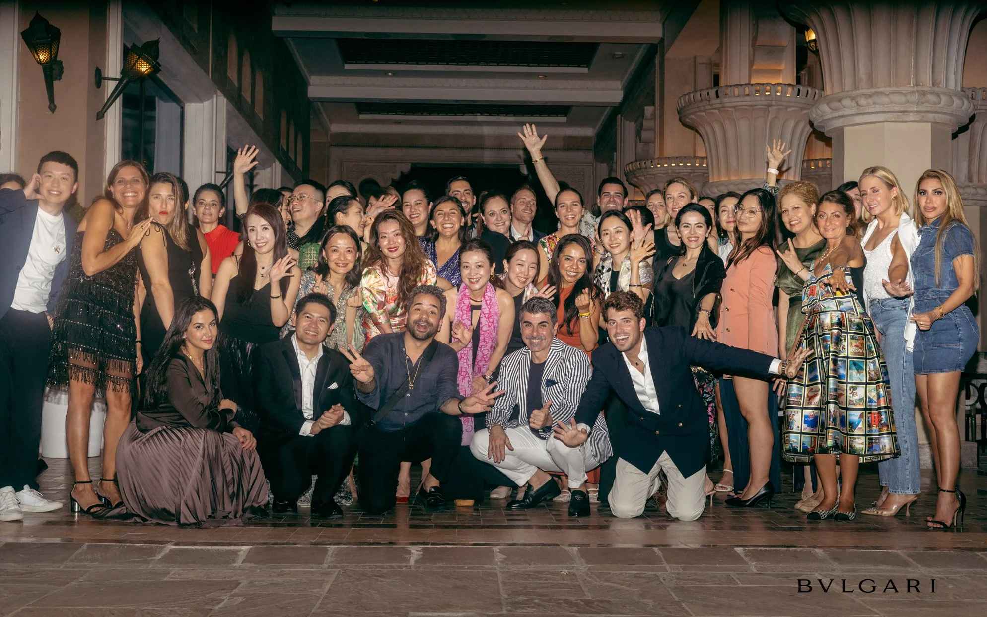 Grupo grande de personas en un evento social sonriendo y posando para la foto, ambiente elegante y decorado.