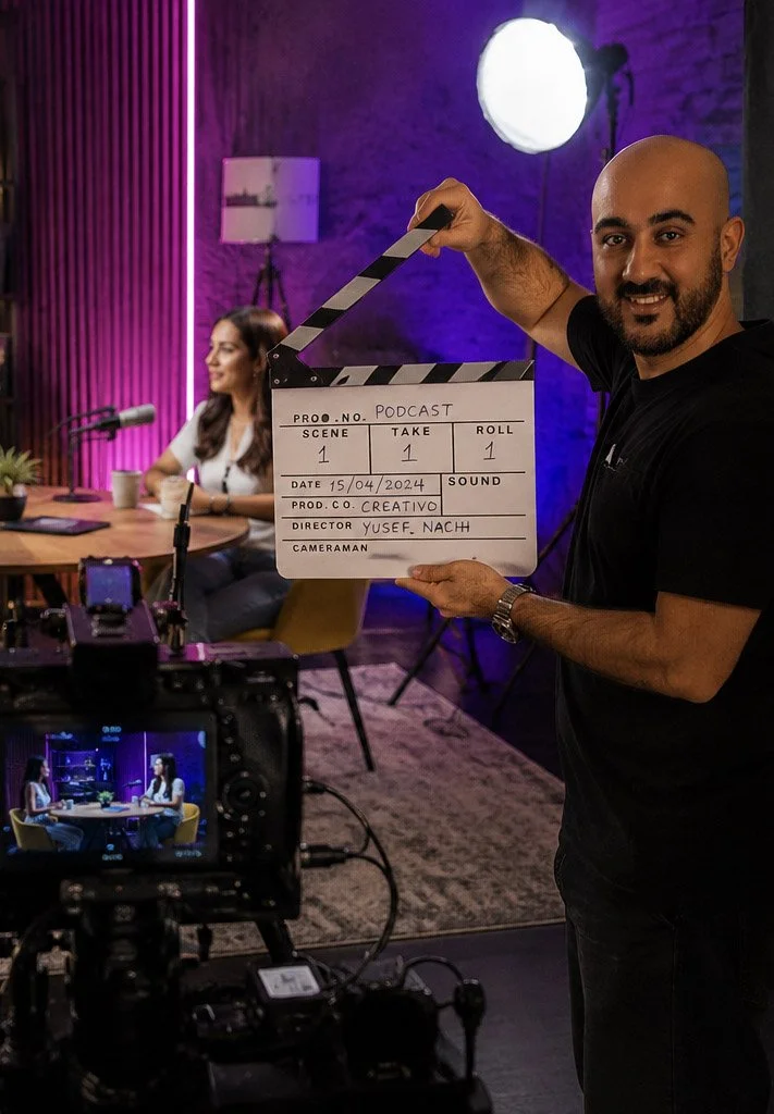 Man holding a clapperboard in a recording studio, with a woman in the background and film equipment producing a podcast in Madrid