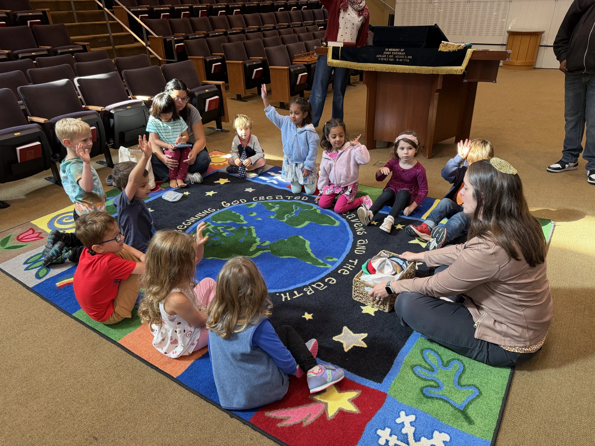 Children drawing and coloring on a large vertical surface with chalk, with leaves on the ground.