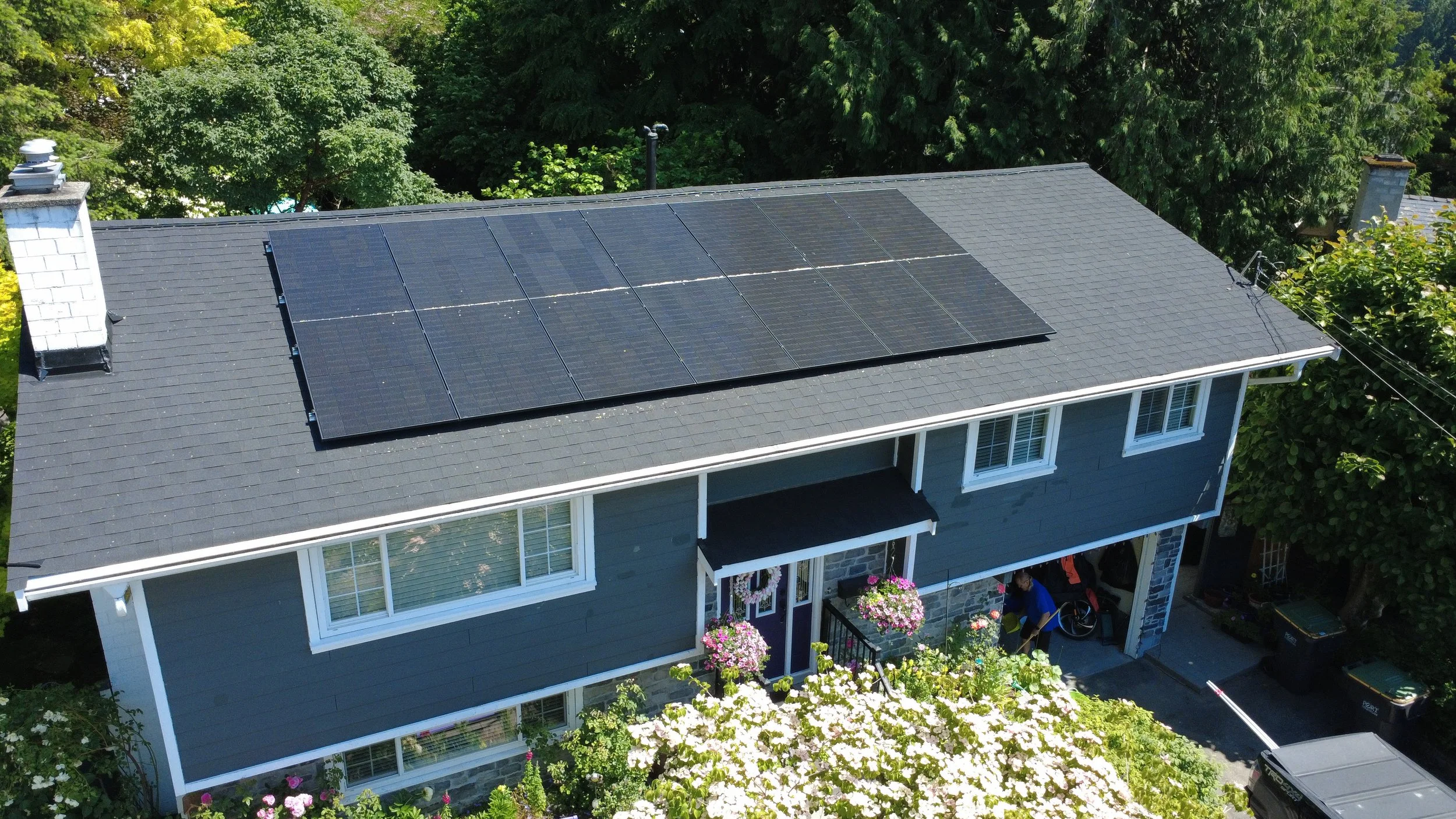 Aerial view of a house with solar panels on the roof, surrounded by trees and plants.