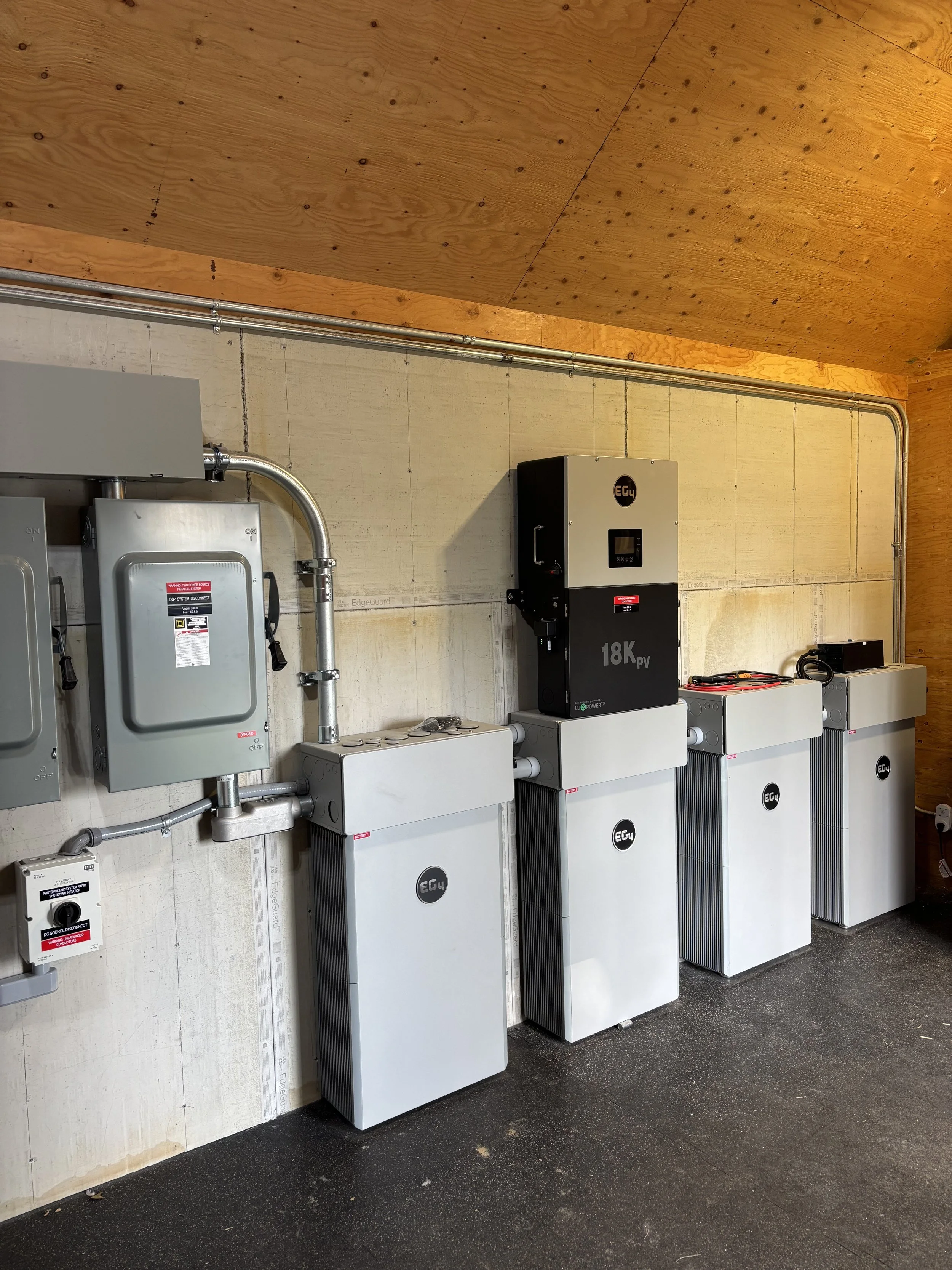 Electrical equipment and solar inverters installed along a concrete wall with a wooden ceiling overhead.