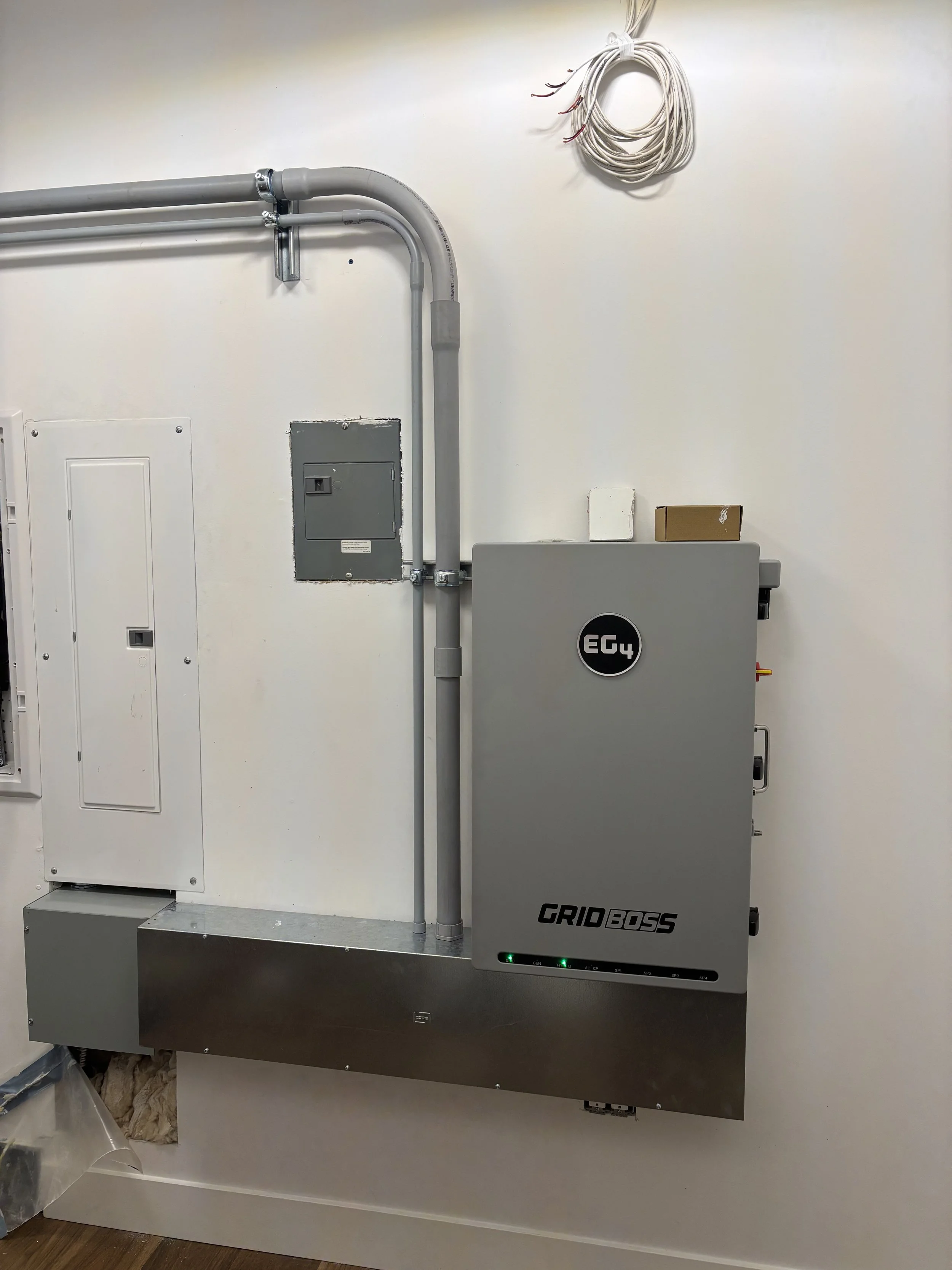Electrical installation panel with gray conduit pipes, a mounted Gray Grid BOSS device, and white wires on the wall.