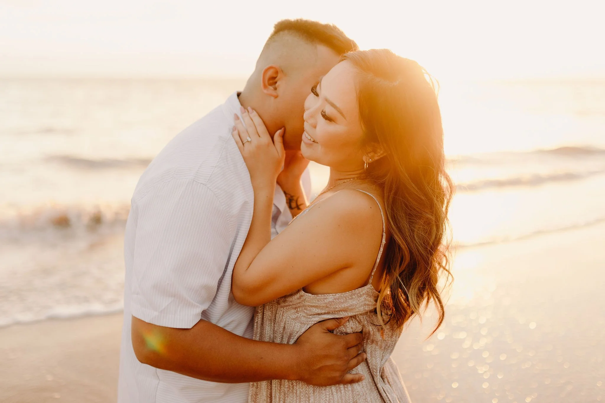 Couple embraces on a beach at golden hour during a romantic Maui engagement session.