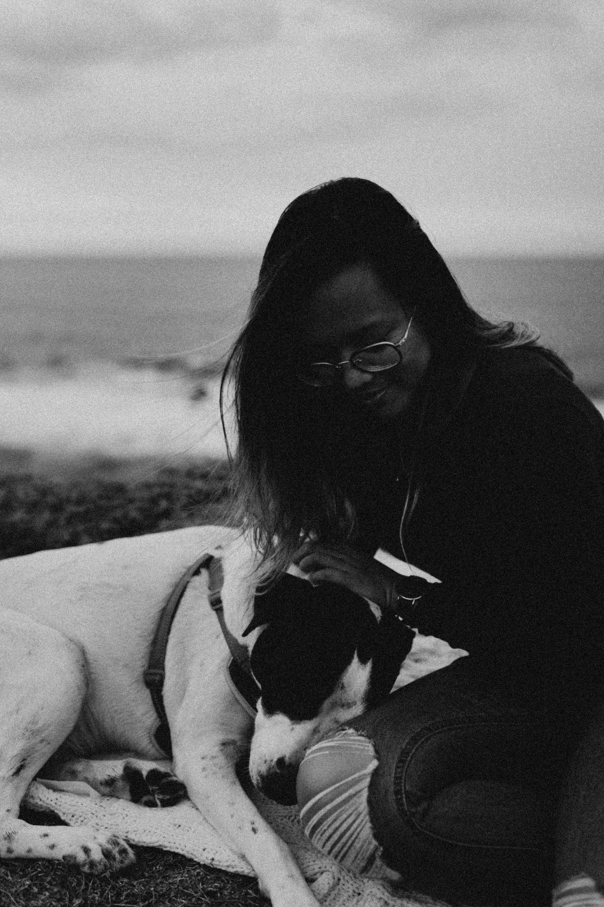 Marie, owner of Marylane Studios, sits on a beach with her dog Rex in a black-and-white portrait.