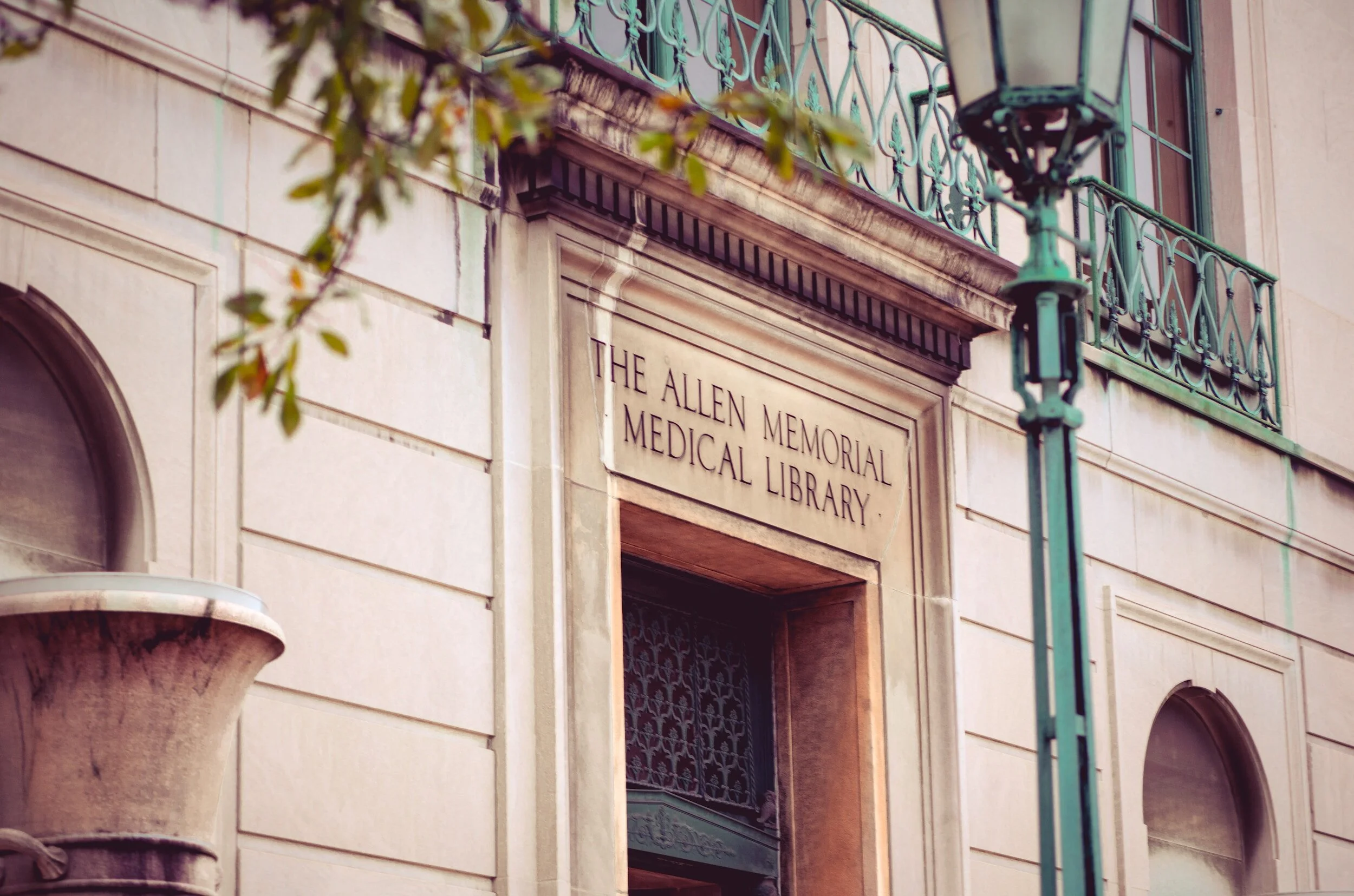 The entrance to the Allen Memorial Medical Library, with a stone sign above the doorway and a green decorative balcony and streetlamp nearby.