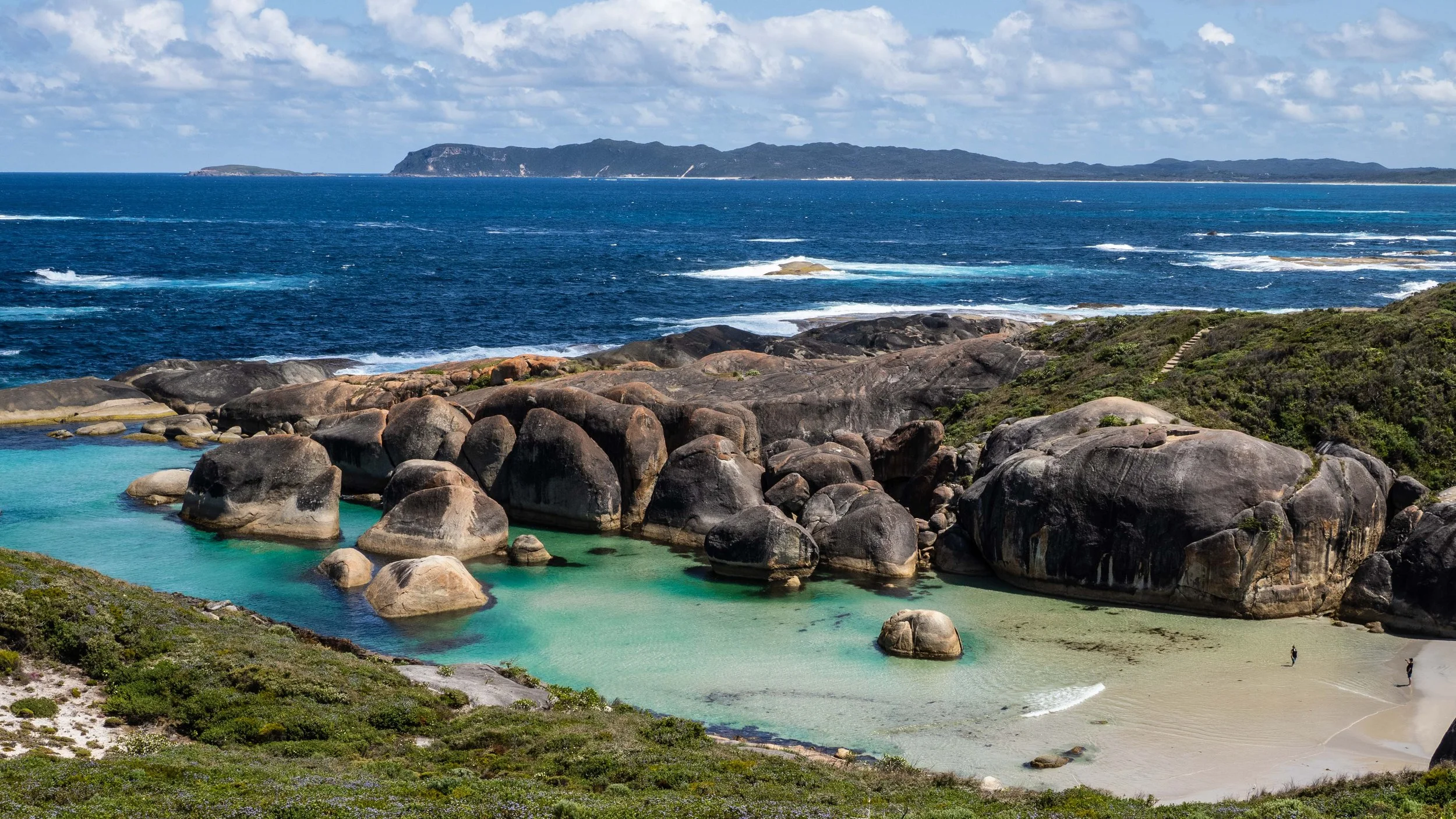 Drone view looking down over Elephant Rocks in Denmark WA with granite boulders and clear blue water.