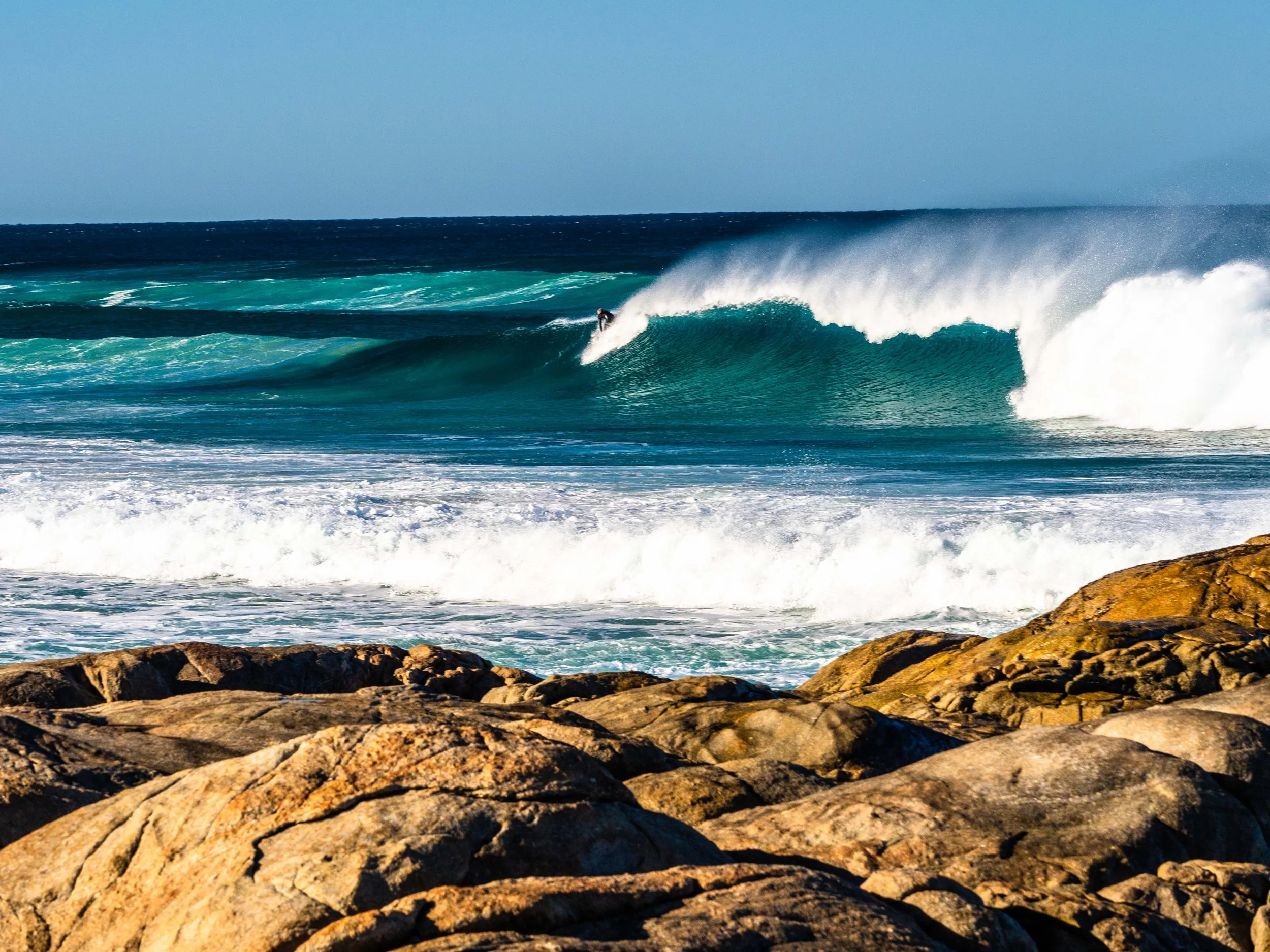 Surfers riding waves at Lights Beach in Denmark Western Australia with rugged coastline and ocean backdrop.