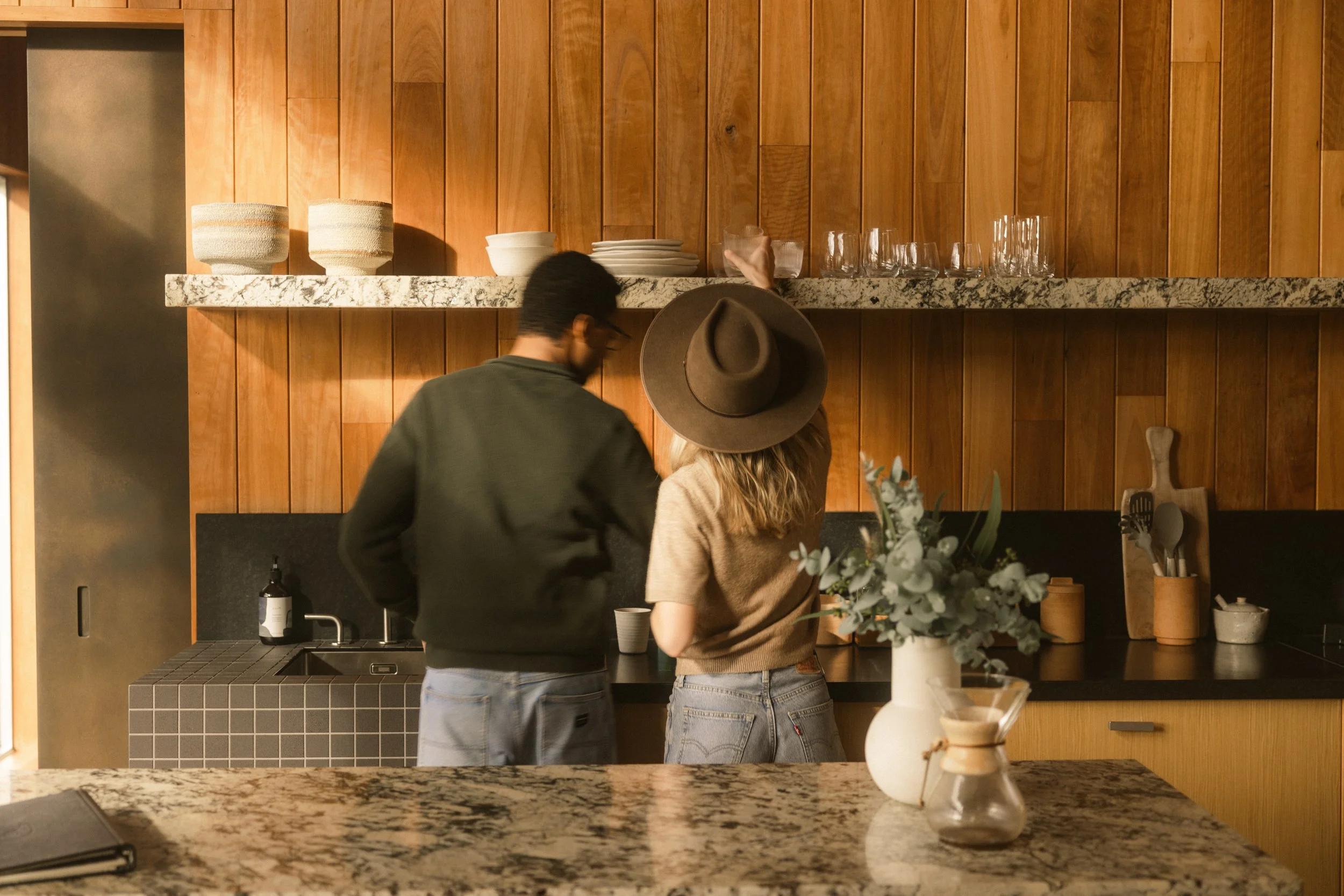 A couple enjoying time together in the kitchen of Cabin Wren at Upland Farm, a peaceful couples retreat in Denmark, Western Australia.