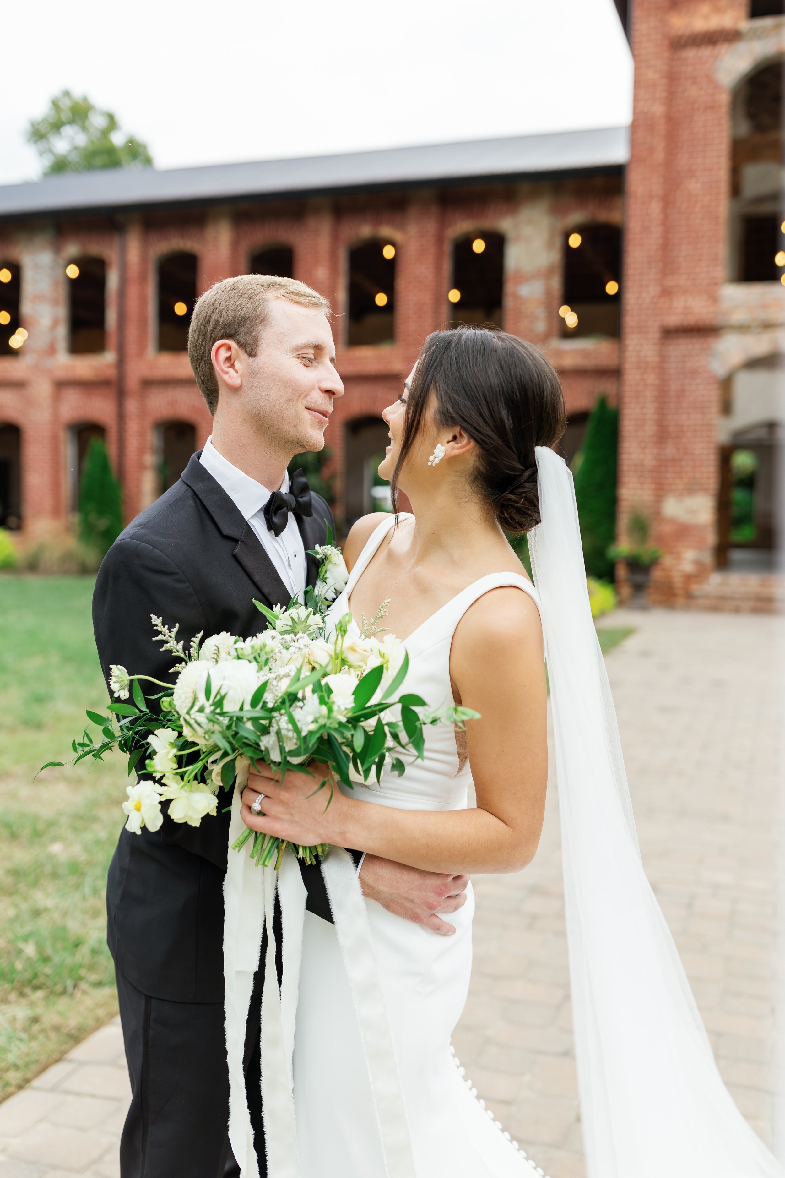 Bride and Groom in front of a brick old cotton mill called Providence Cotton Mill in Maiden, NC - the brides bouquet is all white and green for a garden themed wedding  