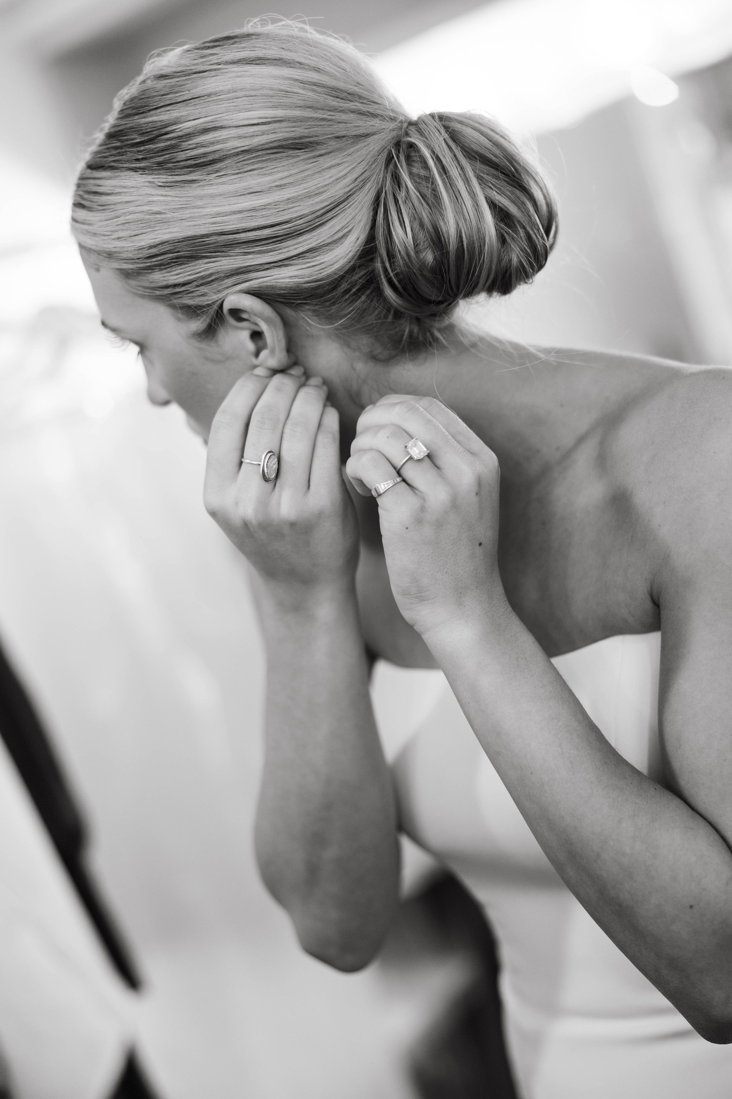 Black and white photo of a woman in an elegant updo adjusting her earring, wearing a strapless dress and ring.