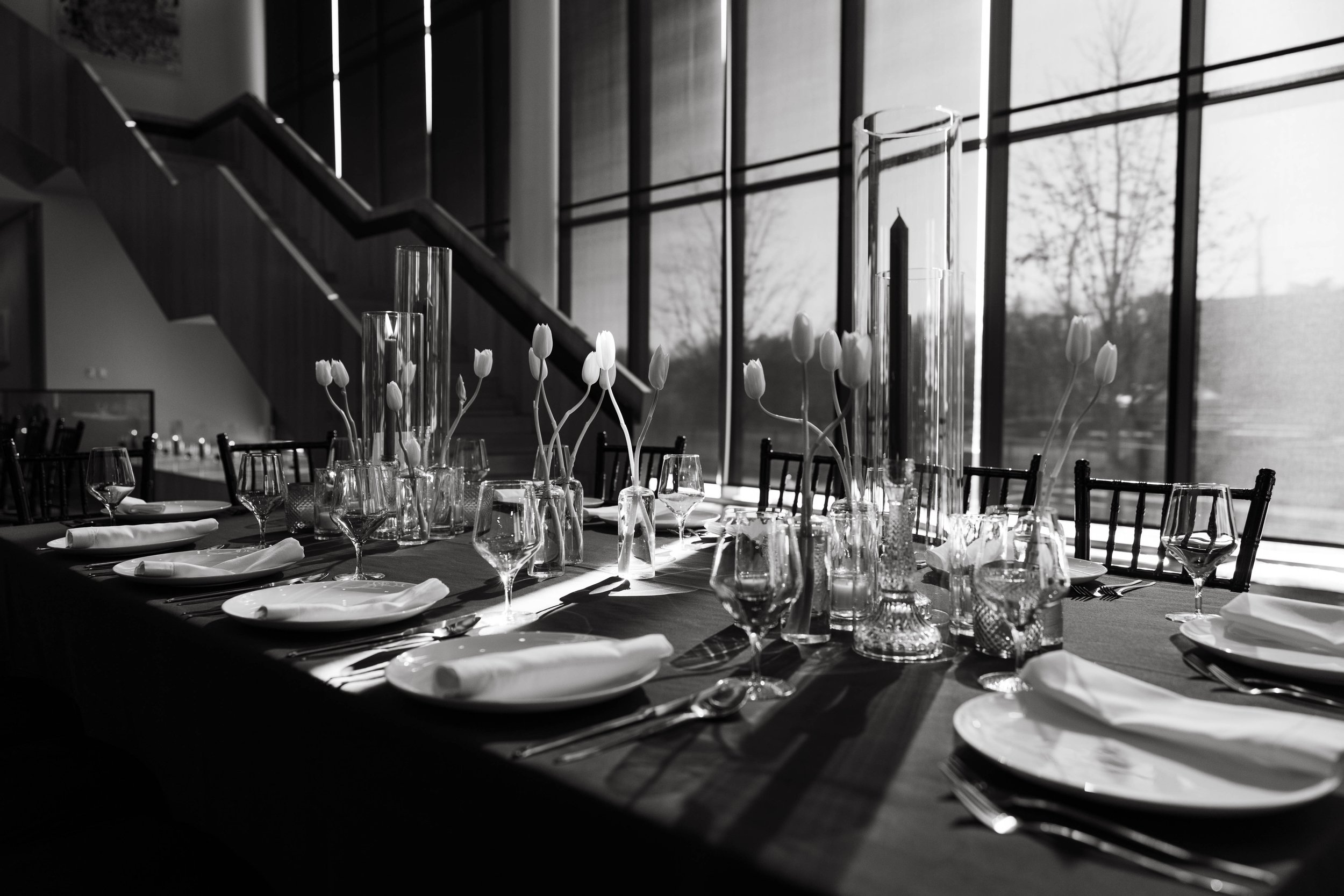 Elegant dining table setup with white tulips, glassware, and silverware in a room with large windows.