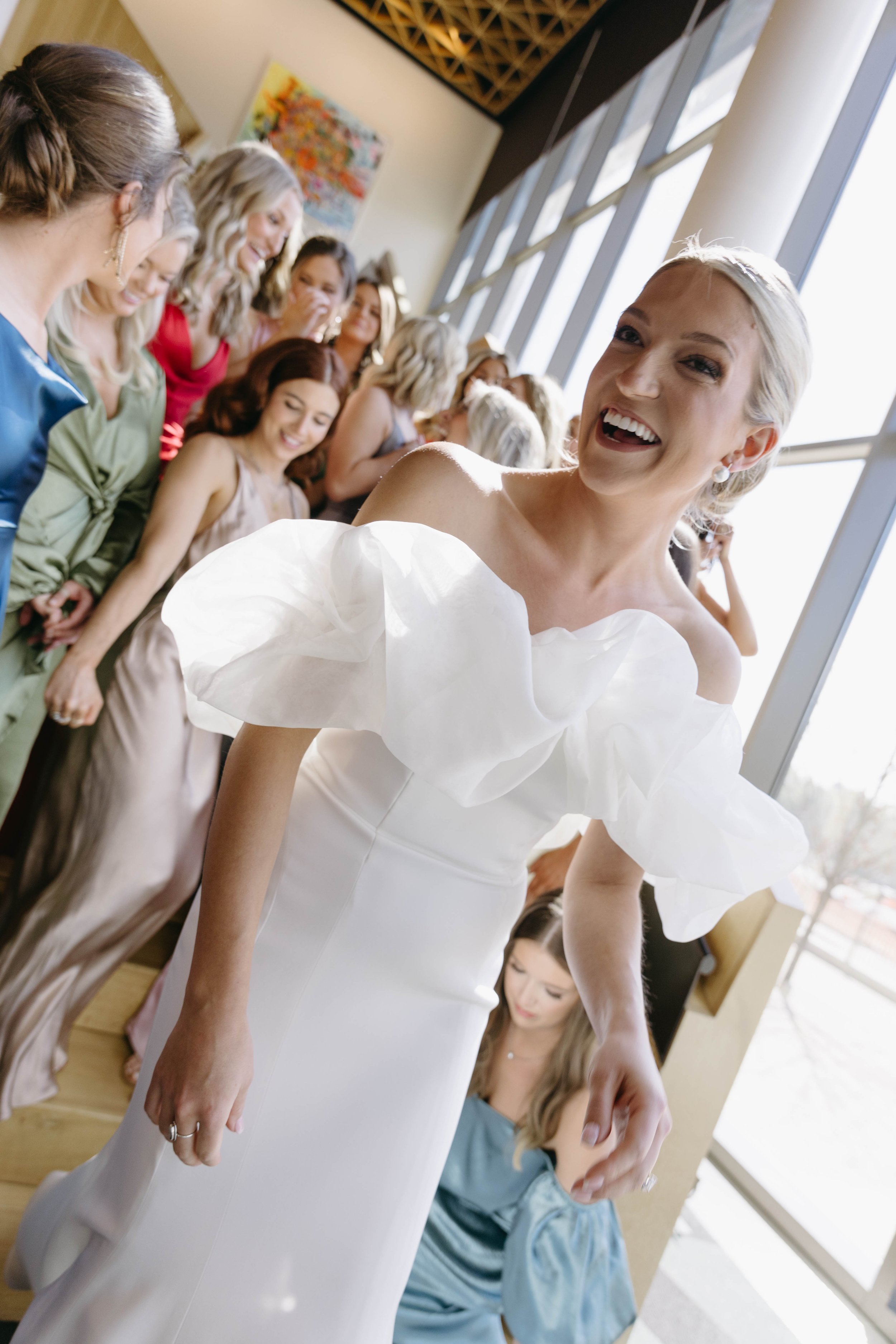 Bride in white dress with bridesmaids in colorful dresses, smiling indoors.